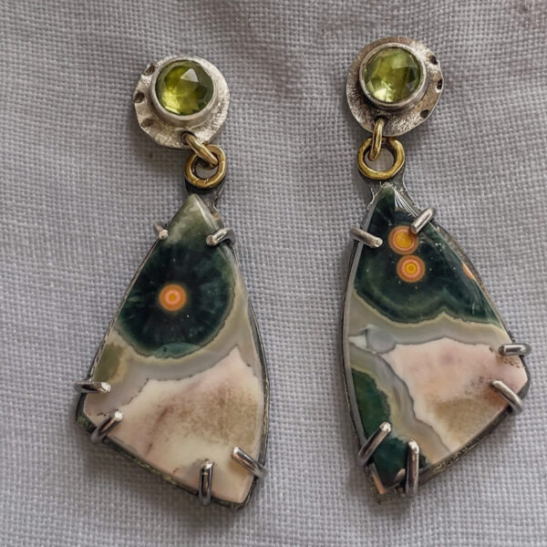 Elegant earrings featuring green peridot gemstones on top and uniquely patterned, triangular ocean jasper stone pendants with silver claw setting.