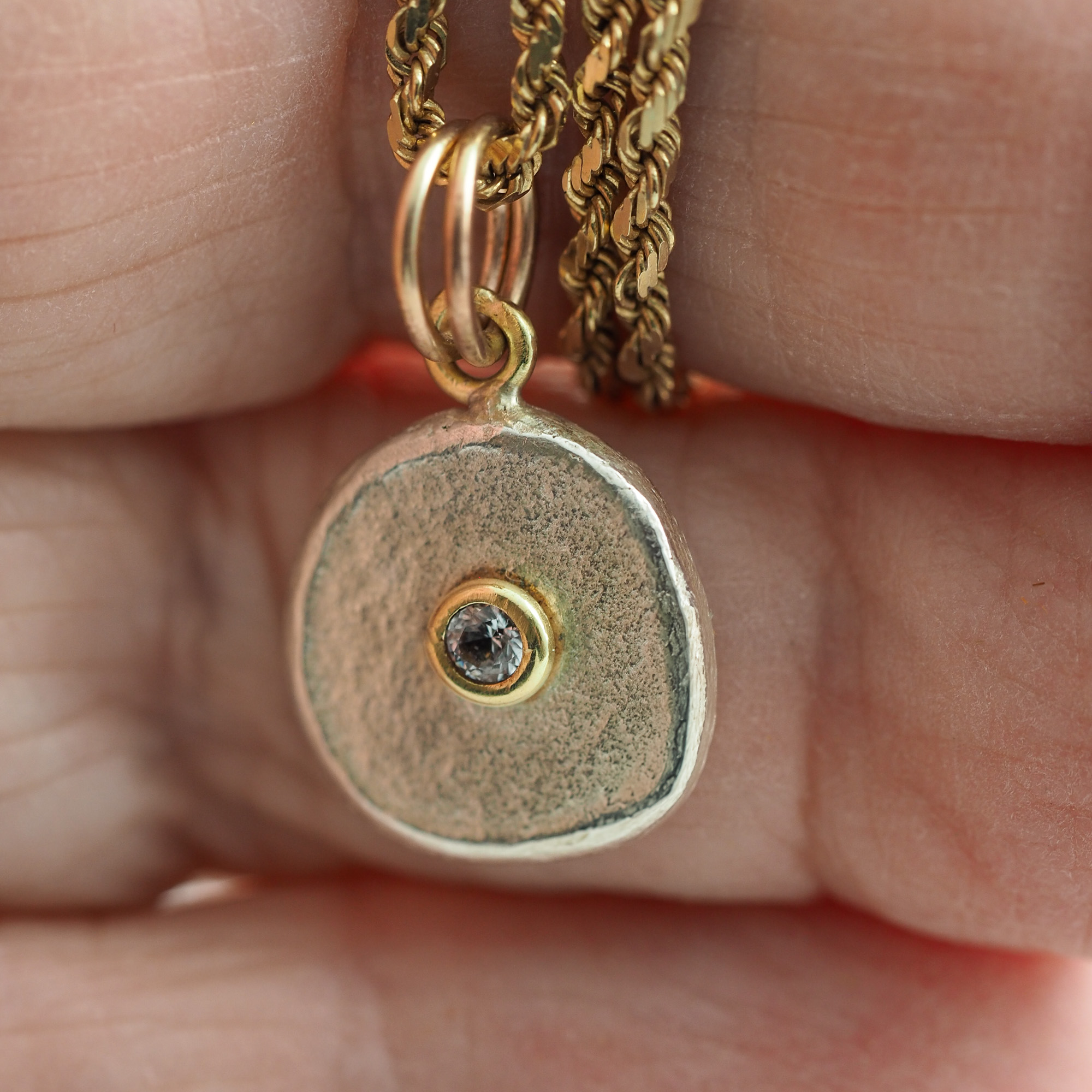 Gold setting with diamond on a round silver disk charm held by the maker's hand