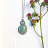 S2C005 Green Goddess with rose on sand web 1x1 opal and green chrysoprase gemstone pendant set in silver on sand with a berry sprig beside it