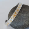 Gold and silver tooled cuff bracelet posed on a gray rock.