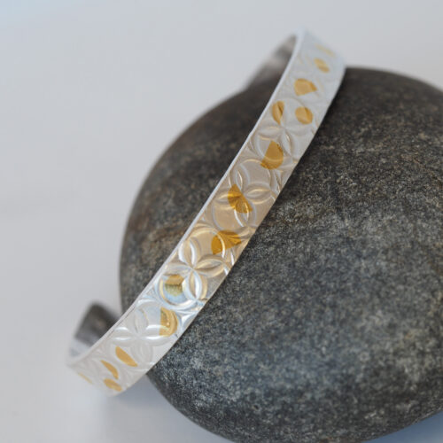 Gold and silver tooled cuff bracelet posed on a gray rock.